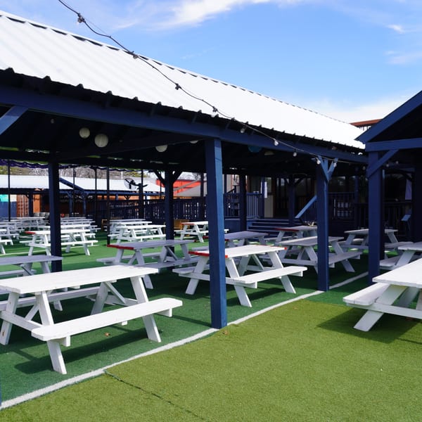 Outdoor dining area at Backyard on Broadway with white picnic tables under a blue covered patio.