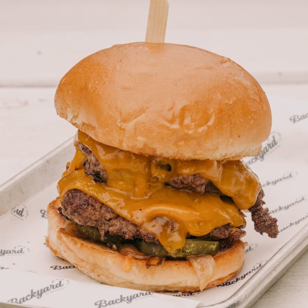 A Backyard on Broadway double cheeseburger with melted cheese, pickles, and onions on a bun.