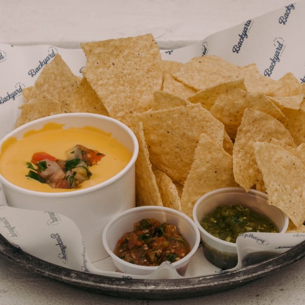 A platter of tortilla chips with a large bowl of queso, salsa, and guacamole.