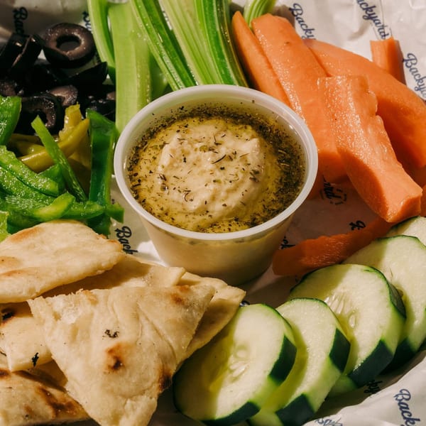 Hummus with pita bread, sliced cucumbers, carrots, celery, green peppers, and black olives.