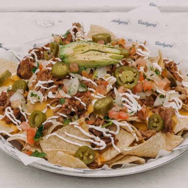 A large plate of Backyard on Broadway nachos with pulled pork, cheese, jalapeños, avocado, and sour cream.