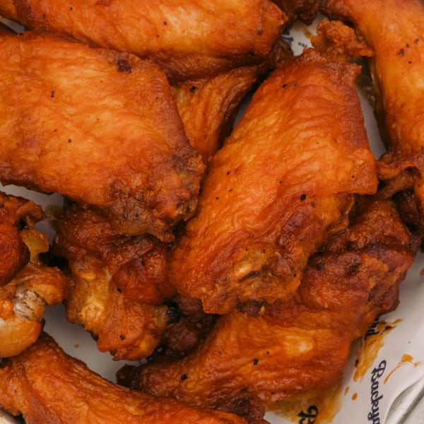 Close-up of crispy, golden-brown chicken wings with visible seasoning, served in a Backyard on Broadway branded container.